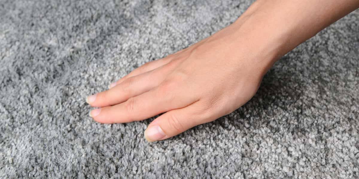 Hand touching soft grey luxury carpet with textured high-pile surface for comfort and durability in upscale interiors.