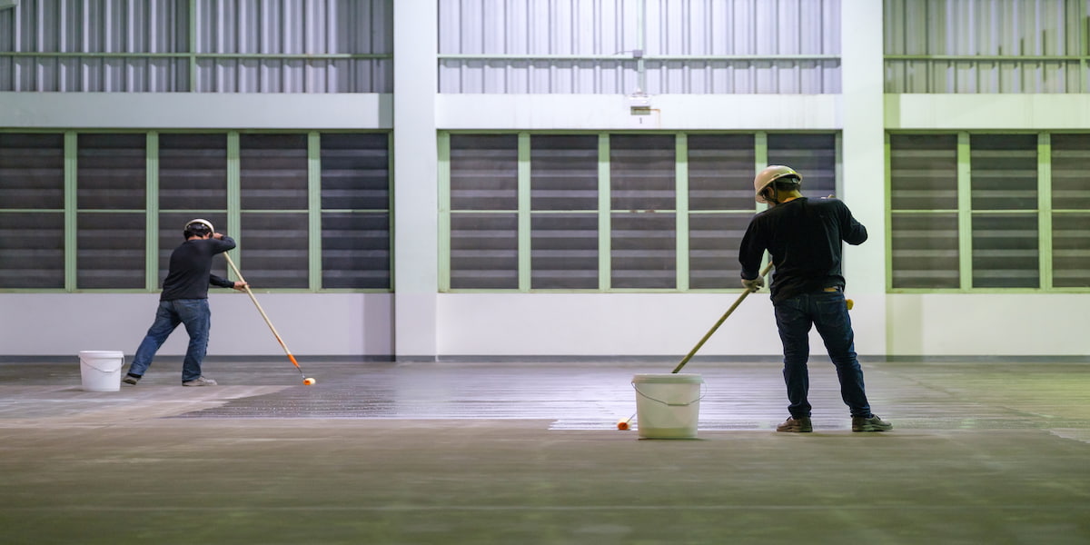 Workers applying commercial epoxy flooring in a large industrial space to create a durable, smooth surface.