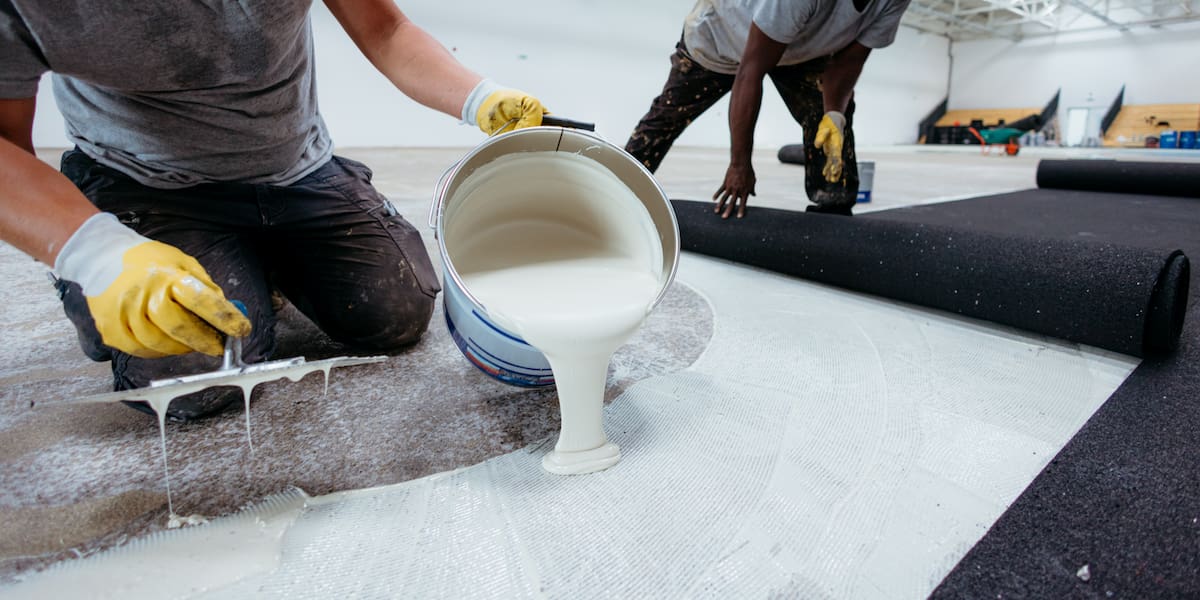 Floor experts applying adhesive for commercial flooring installation, ensuring proper bonding and surface preparation.