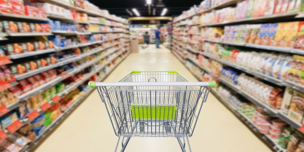 Shopping cart in the aisle of a grocery store with brightly lit shelves, showcasing smooth and durable grocery store flooring designed for high foot traffic and easy maintenance.