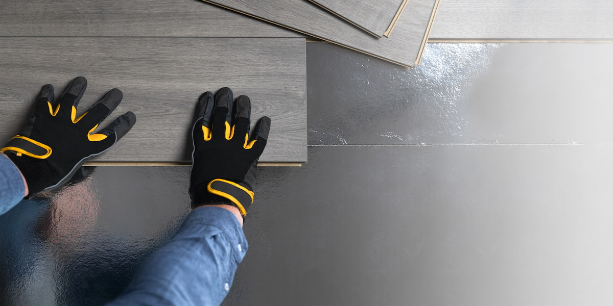 Hands wearing protective gloves installing heavy duty commercial vinyl flooring on a reflective surface, emphasizing durability and professional installation.