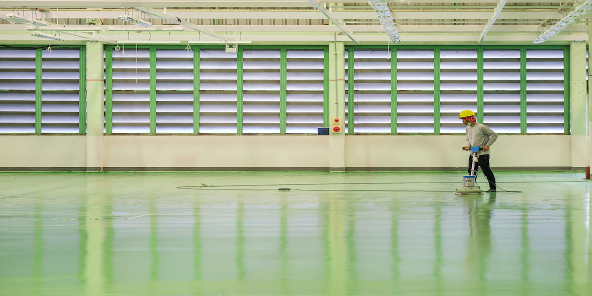 Industrial flooring options: A worker polishes a smooth, green epoxy-coated industrial floor in a spacious facility, showcasing the durability and cleanliness of this flooring choice.