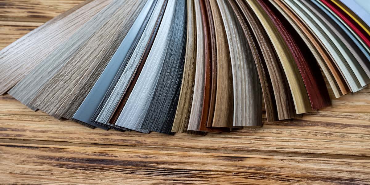 Sample swatches of commercial vinyl flooring in various colors and wood grain patterns displayed on a wooden surface