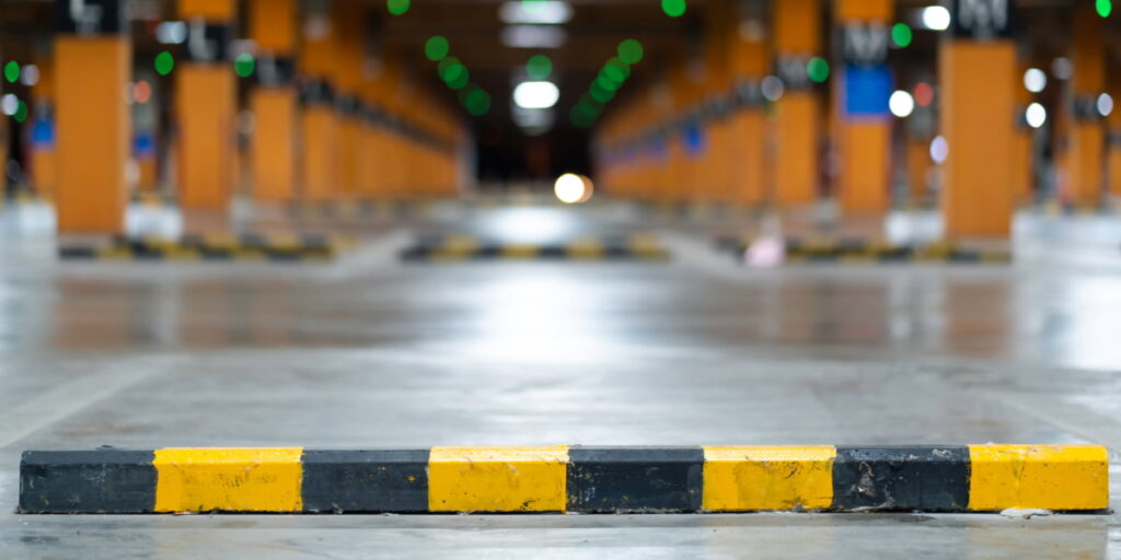 Yellow and black parking stop on concrete garage floor, representing safety flooring contractor expertise in high-liability environments.