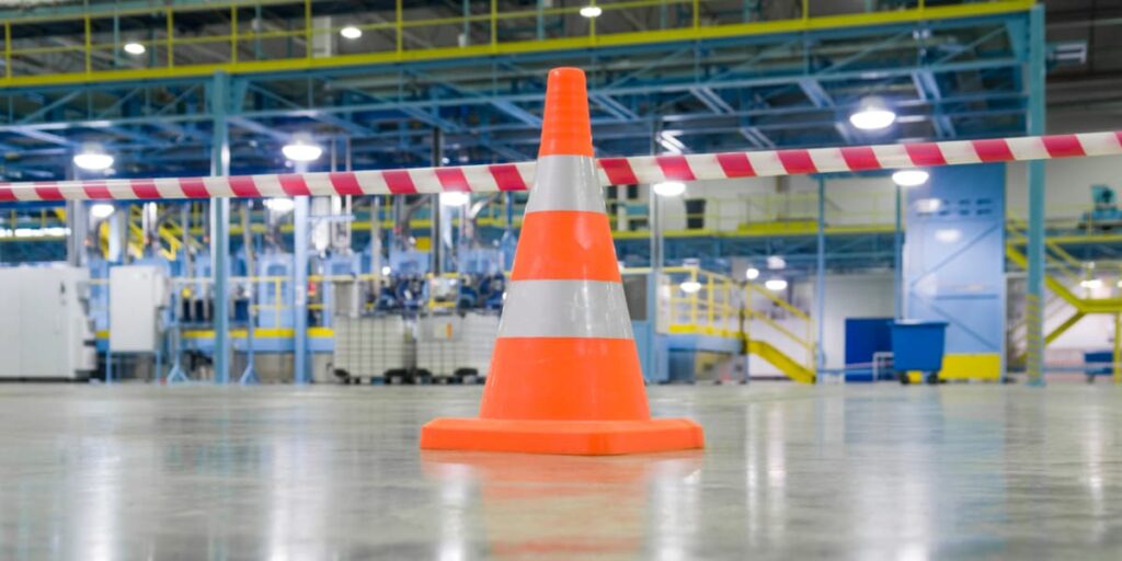 Orange safety cone on polished concrete floor in a factory, symbolizing safety flooring contractor services and OSHA compliance.