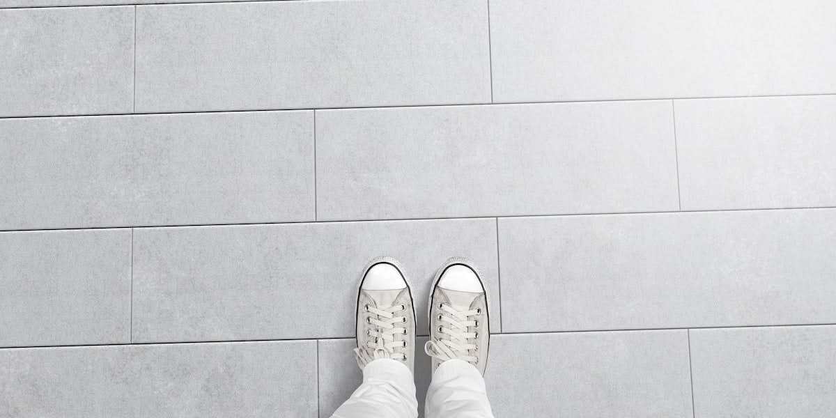 Top-down view of white sneakers on light gray tile floor, representing ANSI slip resistance standards and floor safety compliance